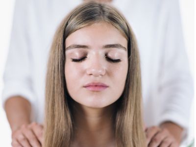 A holistic therapy session where a therapist gently places their hands on a client’s shoulders, symbolizing deep listening and body awareness. The peaceful setting includes candles, plants, healing crystals, and flower remedies, representing personalized healing and self-care.