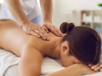 A holistic therapy session where a therapist gently places their hands on a client's upper back and neck, symbolizing the connection between the spine, energy flow, and emotional release. The setting includes soft lighting, healing crystals, and a chart of energy meridians, reinforcing the mind-body connection.