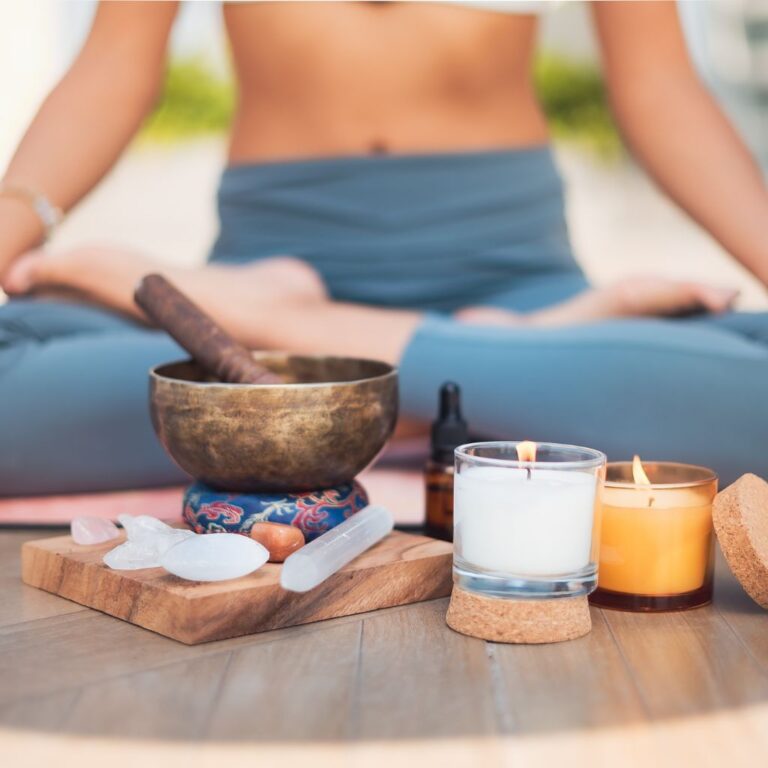 A peaceful therapy space with essential oils, flower remedies, herbal tea, and an affirmation card, symbolizing emotional and energy healing. A woman sits by a window with sunlight, holding her heart in a self-care moment.